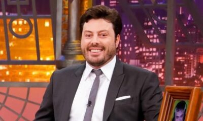 Danilo Gentili, de terno e gravata, sorri para a câmera em cenário de televisão