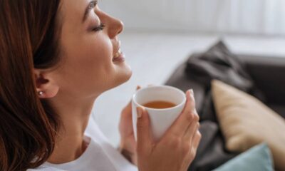 Mulher sorrindo com olhos fechados, segurando uma xícara de chá quente em ambiente doméstico