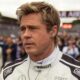 Brad Pitt, cabelo loiro, em uniforme de corrida branco, com fone de ouvido