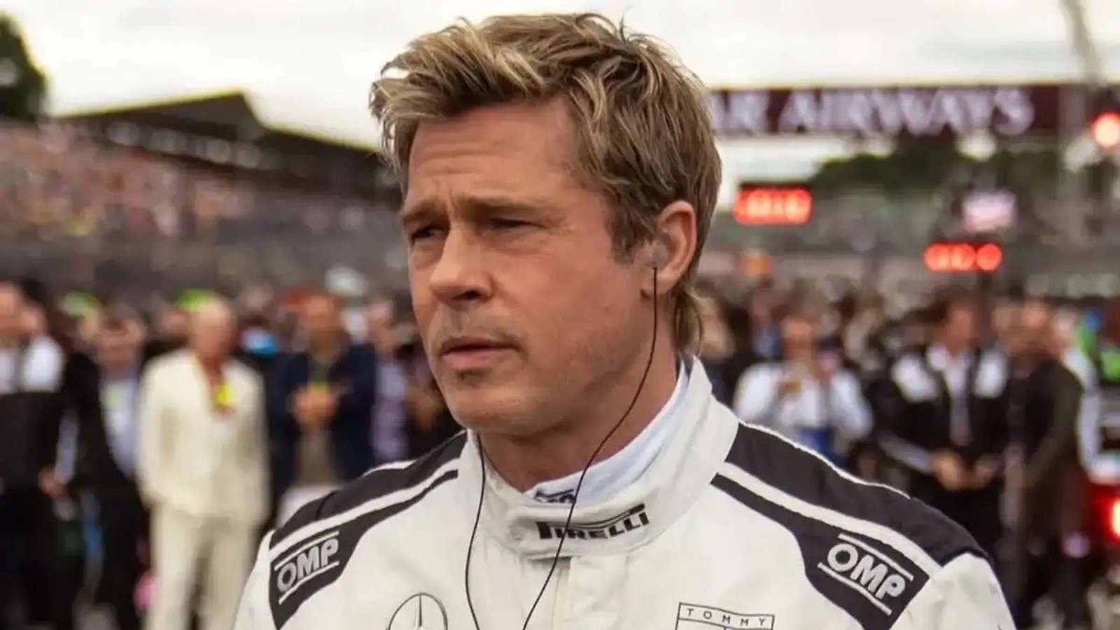 Brad Pitt, cabelo loiro, em uniforme de corrida branco, com fone de ouvido