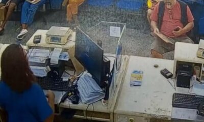 Balcão de atendimento de agência postal com funcionária, monitor, teclado e cliente aguardando