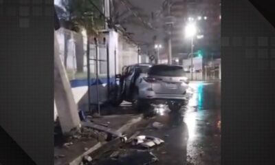 SUV prateado chocado contra muro de prédio à noite, com porta aberta e destroços