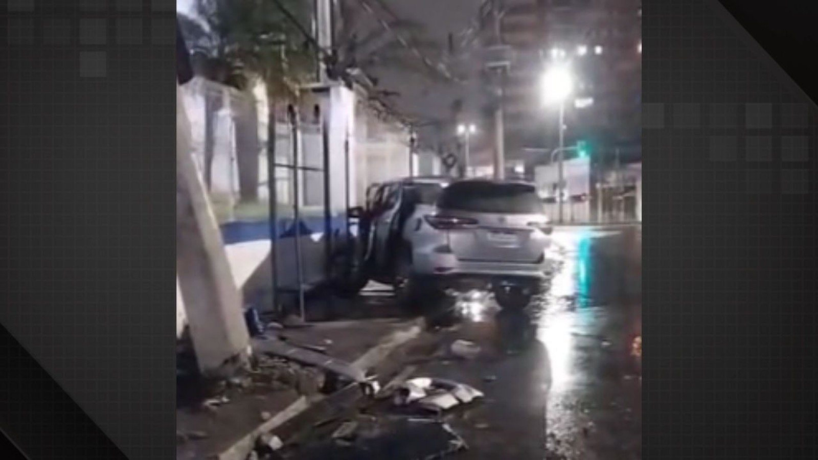 SUV prateado chocado contra muro de prédio à noite, com porta aberta e destroços