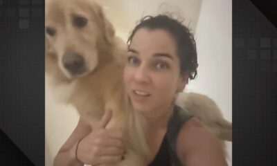 Mulher de cabelos escuros e molhados carregando um golden retriever nos ombros olhando para a câmera