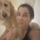 Mulher de cabelos escuros e molhados carregando um golden retriever nos ombros olhando para a câmera