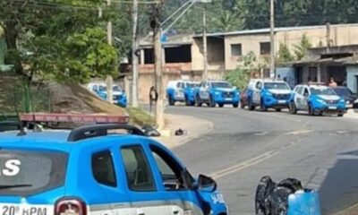 Fila de viaturas policiais azuis e brancas do 20º BPM em rua de Nova Iguaçu