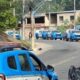 Fila de viaturas policiais azuis e brancas do 20º BPM em rua de Nova Iguaçu