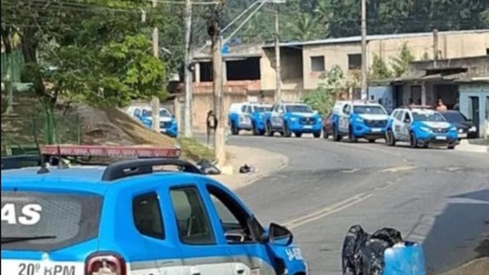 Fila de viaturas policiais azuis e brancas do 20º BPM em rua de Nova Iguaçu