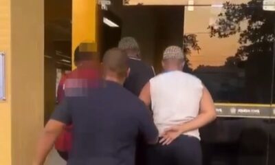 Agentes conduzem homens à entrada de prédio da Polícia Civil ao entardecer
