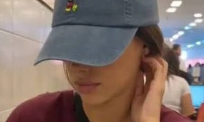 Bruna Biancardi de boné azul e camiseta vinho cobrindo o rosto, mão na orelha
