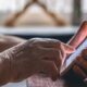 Close-up de mãos enrugadas de uma pessoa idosa segurando e digitando em um smartphone