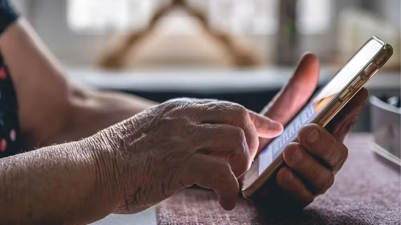 Close-up de mãos enrugadas de uma pessoa idosa segurando e digitando em um smartphone