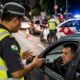 Policial com colete amarelo aborda motorista em carro à noite durante blitz