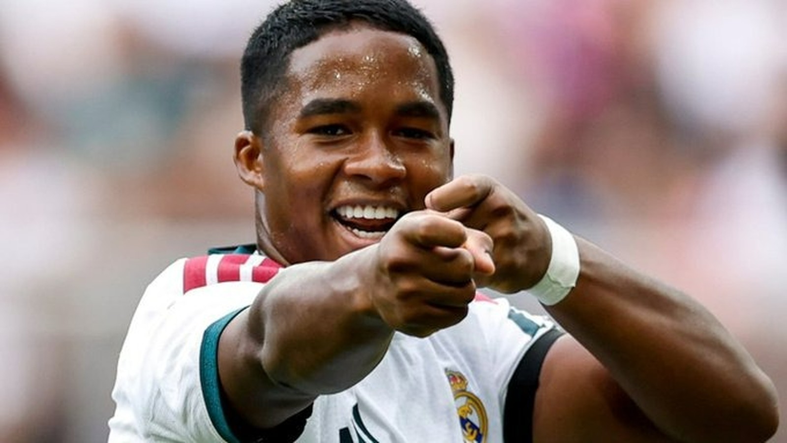Jogador Endrick, com a camisa do Real Madrid, sorri e aponta para frente