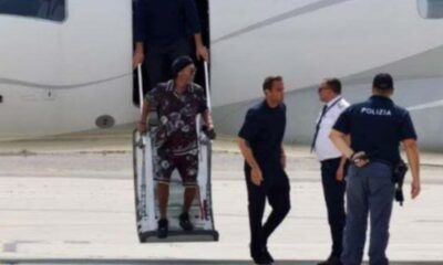Ronaldinho Gaúcho descendo escada de avião com seguranças e policial no tarmac