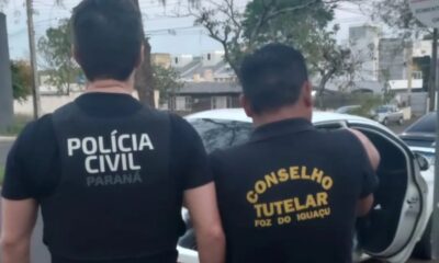 Homens da Polícia Civil e Conselho Tutelar, de costas, perto de carro branco em rua