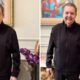 Faustão sorri e gesticula em vídeo, vestindo jaqueta preta, com quadro e flores ao fundo
