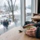 Pessoa segura tigela de sopa em mesa de madeira, janela com gotas de chuva e neve lá fora