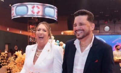 Mulher loira rindo e homem de terno sorrindo em evento com tema náutico