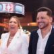 Mulher loira rindo e homem de terno sorrindo em evento com tema náutico