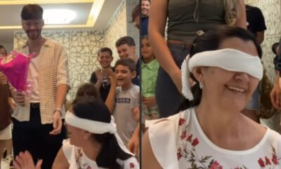 Jovem sorridente com buquê de flores e mulher vendada sorrindo em reencontro emocionante
