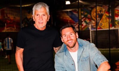 Lionel Messi sorri ao lado de homem de cabelo grisalho em quadra de futebol coberta
