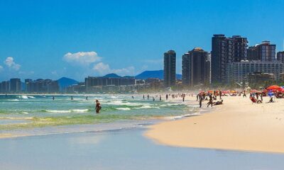 Praia movimentada com mar agitado, areia, pessoas, guarda-sóis coloridos e prédios altos