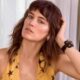 Bianca Bin, cabelo castanho e franja, blusa amarela com estrelas, mão na cabeça
