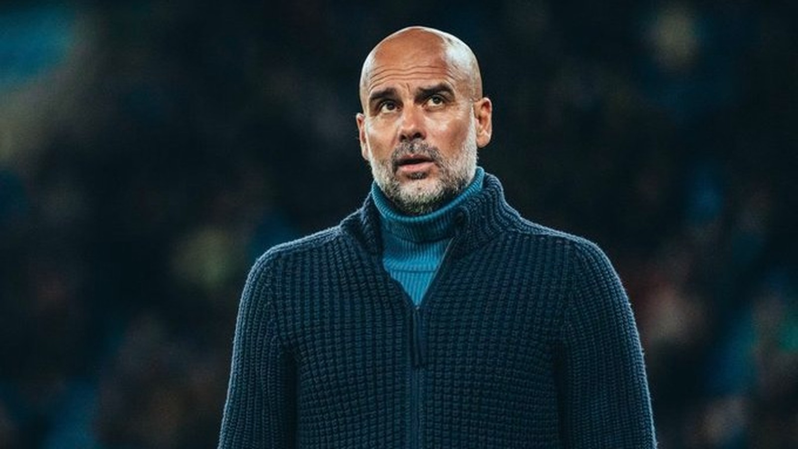 Pep Guardiola, careca e barbudo, em suéter azul escuro, com olhar pensativo