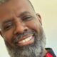 Rosto de homem negro sorridente com barba e cabelo grisalho