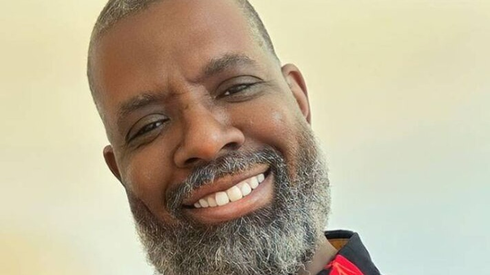 Rosto de homem negro sorridente com barba e cabelo grisalho