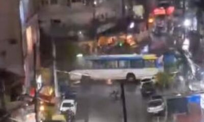 Visão noturna borrada de rua com ônibus branco e azul, veículos e luzes urbanas