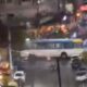 Visão noturna borrada de rua com ônibus branco e azul, veículos e luzes urbanas