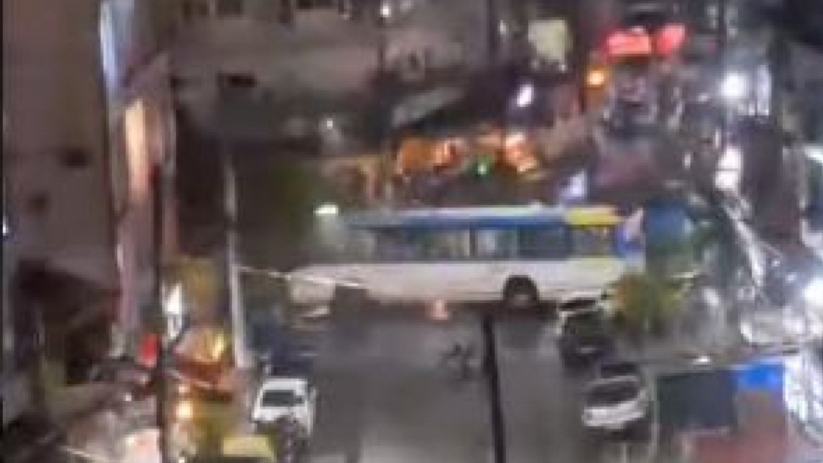 Visão noturna borrada de rua com ônibus branco e azul, veículos e luzes urbanas