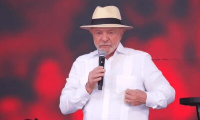 Luiz Inácio Lula da Silva, com chapéu e camisa branca, fala em microfone.