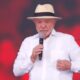 Luiz Inácio Lula da Silva, com chapéu e camisa branca, fala em microfone.