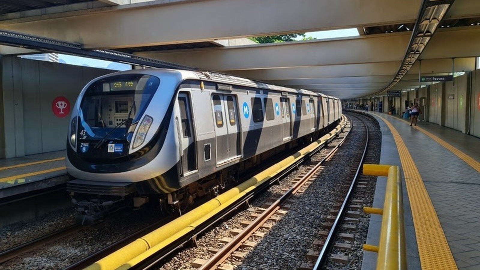 Trem moderno do MetrôRio parado em plataforma curva da estação Pavuna com pessoas ao fundo
