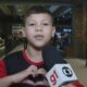 Menino sorridente em shopping faz coração com as mãos para microfone G1