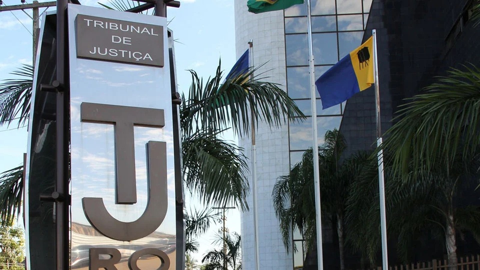 Sinal do Tribunal de Justiça com letras TJ, palmeiras e bandeiras do Brasil e Rondônia