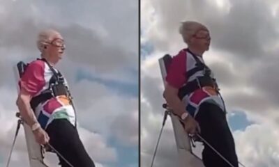 Mulher idosa com óculos e roupa colorida em harness contra céu nublado, praticando wing walking