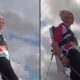 Mulher idosa com óculos e roupa colorida em harness contra céu nublado, praticando wing walking