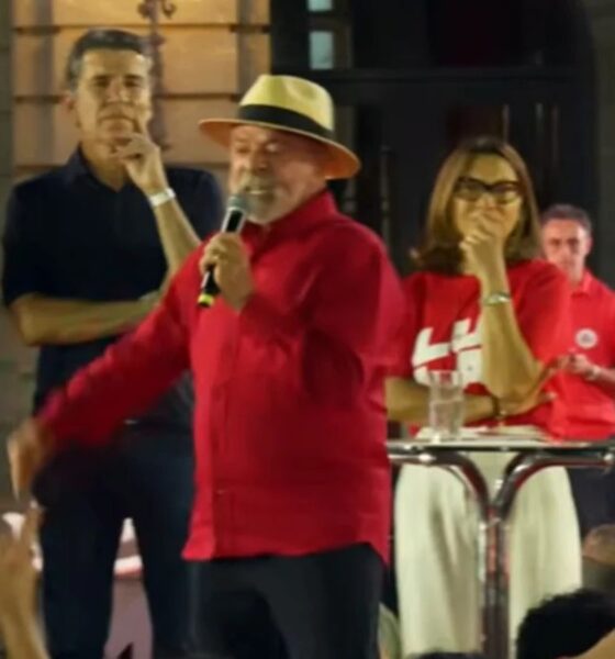 Lula, de camisa vermelha e chapéu, fala ao microfone em palco com outras pessoas