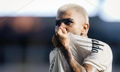Close-up de Gabigol, cabelo loiro, puxa camisa branca sobre o nariz, suado