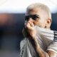 Close-up de Gabigol, cabelo loiro, puxa camisa branca sobre o nariz, suado