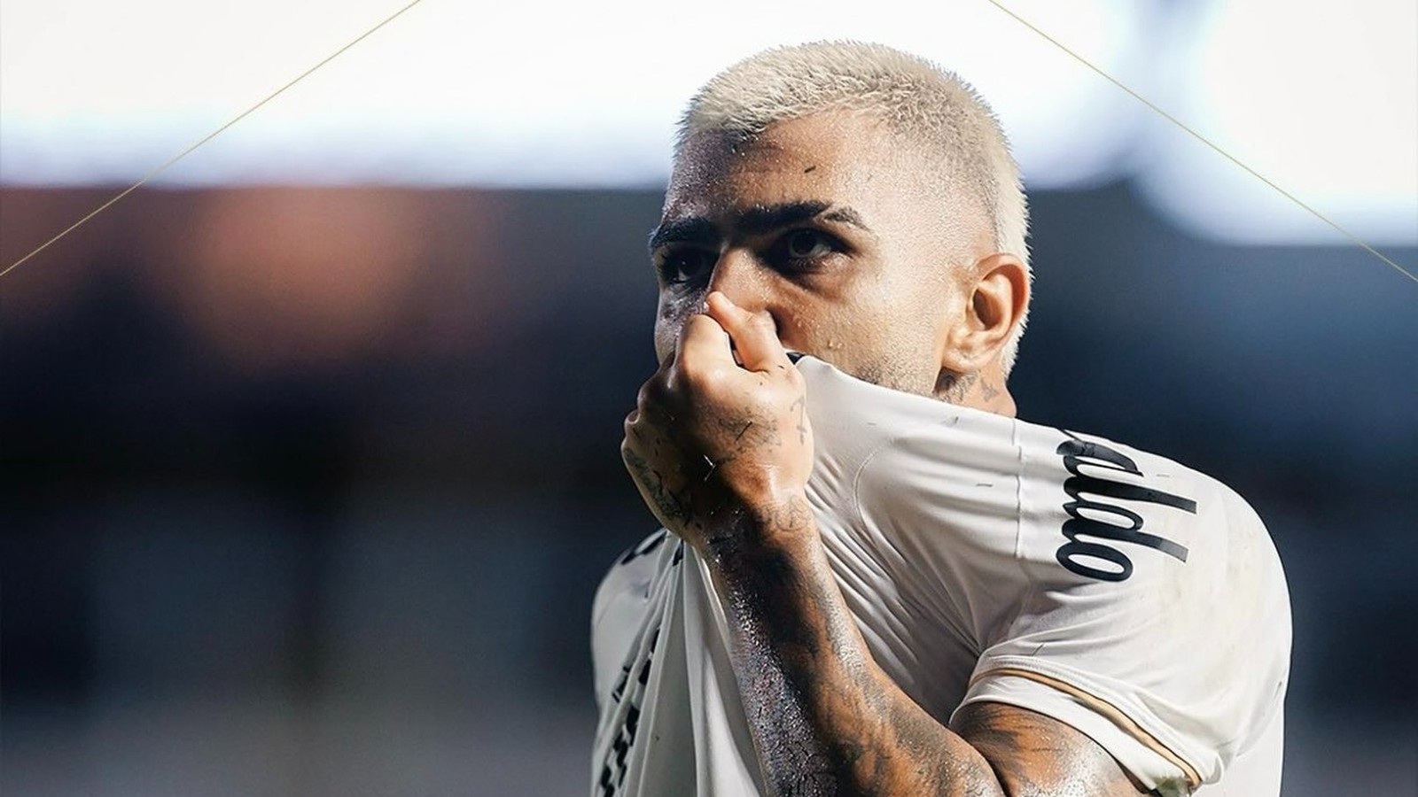 Close-up de Gabigol, cabelo loiro, puxa camisa branca sobre o nariz, suado