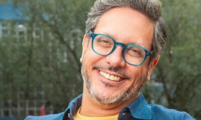 Lúcio Mauro Filho sorrindo, de óculos azuis, cabelo grisalho e barba em ambiente externo