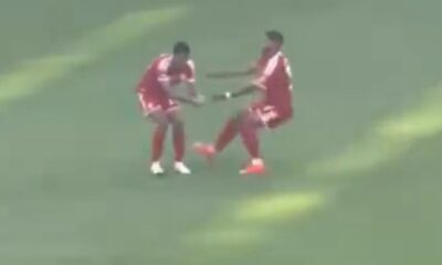 Dois jogadores em uniformes vermelhos no campo de futebol, um apoiando o outro