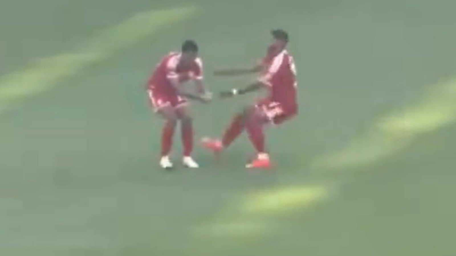 Dois jogadores em uniformes vermelhos no campo de futebol, um apoiando o outro