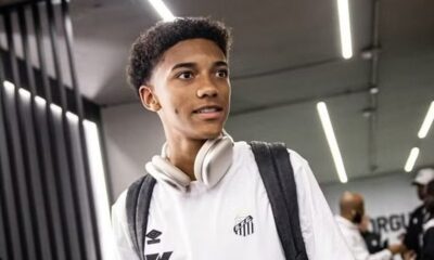 Jovem com cabelo cacheado, camisa do Santos, fones de ouvido no pescoço e mochila