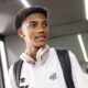 Jovem com cabelo cacheado, camisa do Santos, fones de ouvido no pescoço e mochila
